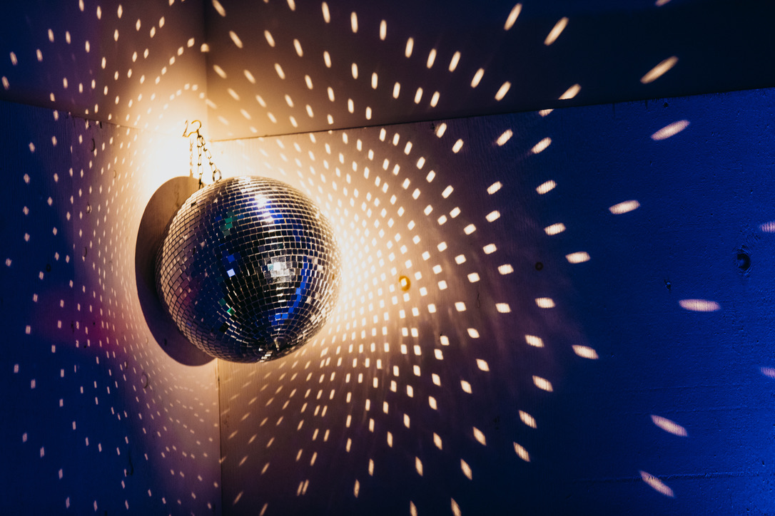 A mirrorball, hung in a corner, casts hundreds of shining points of reflected light along the wall and ceiling. 