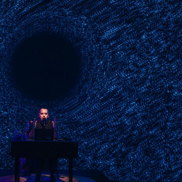 Stewart Legere, sitting at a table. Behind him is a projection of a blackhole.