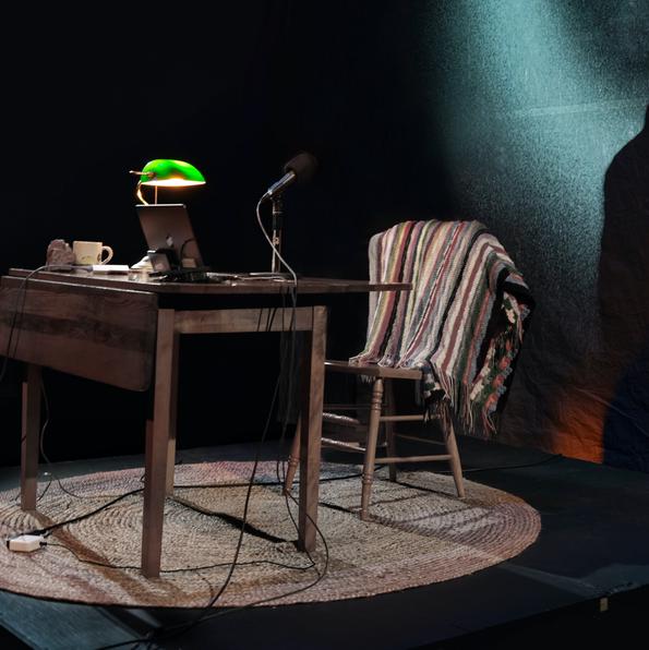 to the left, a chair with a blanket, a table, a banker's lamp. behind it, a large glowing blue circle on the wall. a shadow of a man on the wall. 